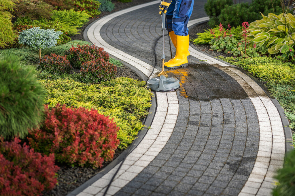 Worker Power Washing Residential Garden Pathway Using Professional Pressure Washer and Surface Attachment